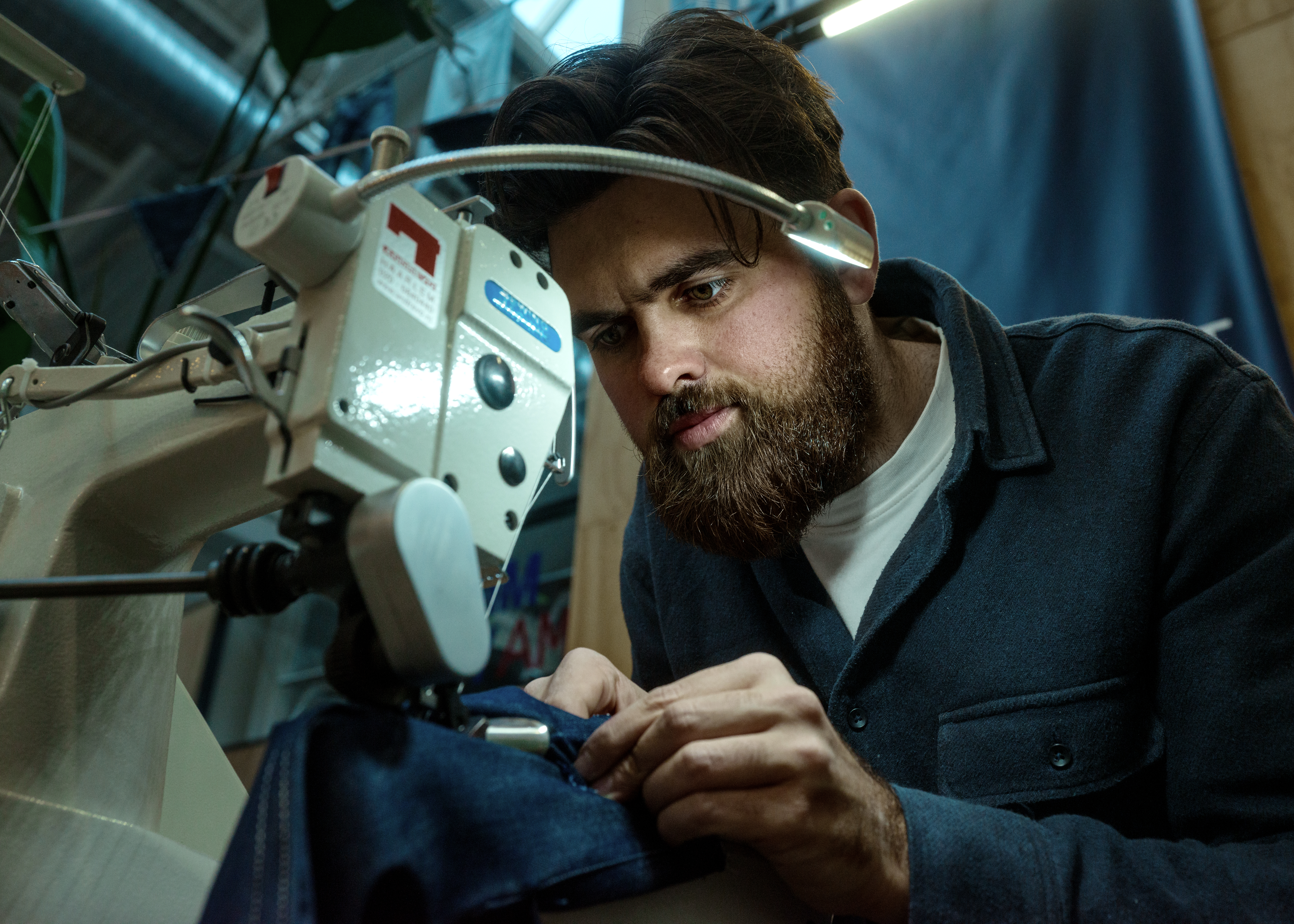 Craftsman at an industrial sewing machine, feeding dark denim through